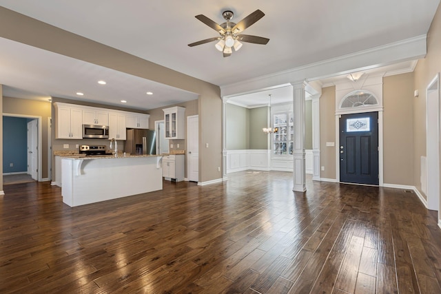 interior space featuring ornamental molding, ceiling fan with notable chandelier, dark wood-type flooring, and decorative columns