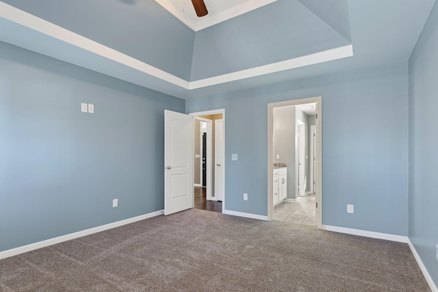 interior space with a tray ceiling, ensuite bath, light colored carpet, and ceiling fan