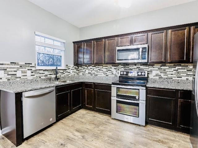 kitchen featuring light stone countertops, appliances with stainless steel finishes, light wood-type flooring, and dark brown cabinetry