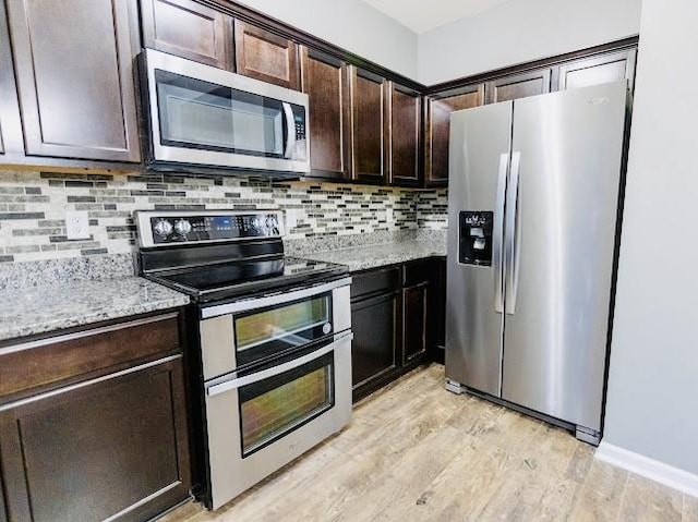 kitchen featuring dark brown cabinetry, light stone counters, light wood-type flooring, stainless steel appliances, and backsplash