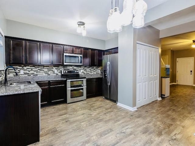 kitchen with dark brown cabinetry, sink, decorative light fixtures, appliances with stainless steel finishes, and light stone countertops