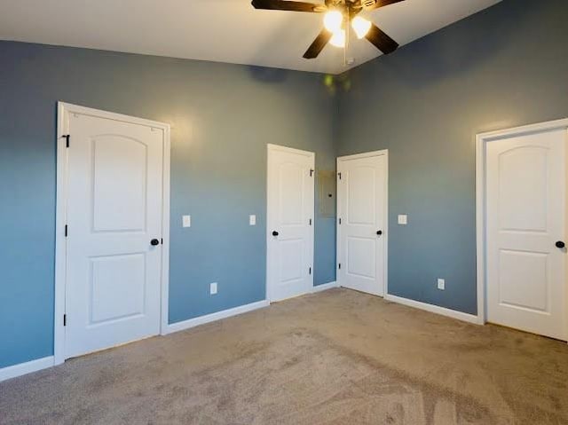 unfurnished bedroom featuring multiple closets, lofted ceiling, light colored carpet, and ceiling fan