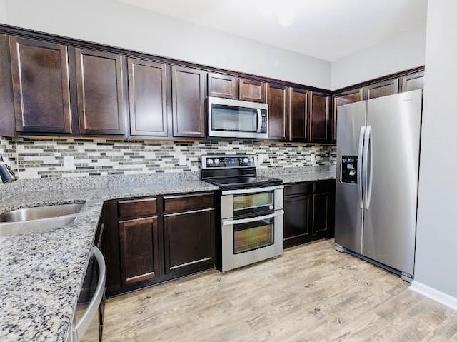 kitchen featuring sink, light hardwood / wood-style flooring, appliances with stainless steel finishes, dark brown cabinetry, and light stone countertops