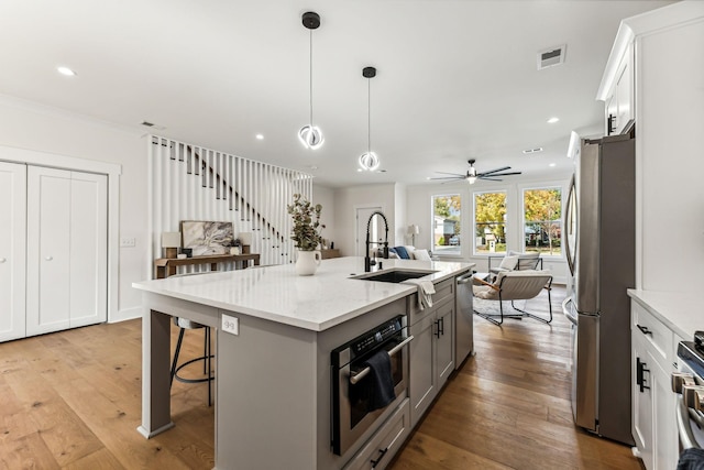 kitchen featuring appliances with stainless steel finishes, decorative light fixtures, sink, a kitchen island with sink, and light stone countertops