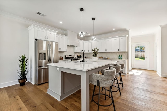 kitchen featuring white cabinets, backsplash, stainless steel appliances, custom range hood, and a center island with sink