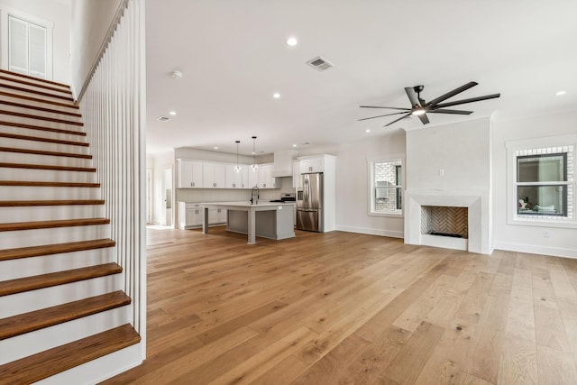 unfurnished living room with ceiling fan, sink, and light wood-type flooring