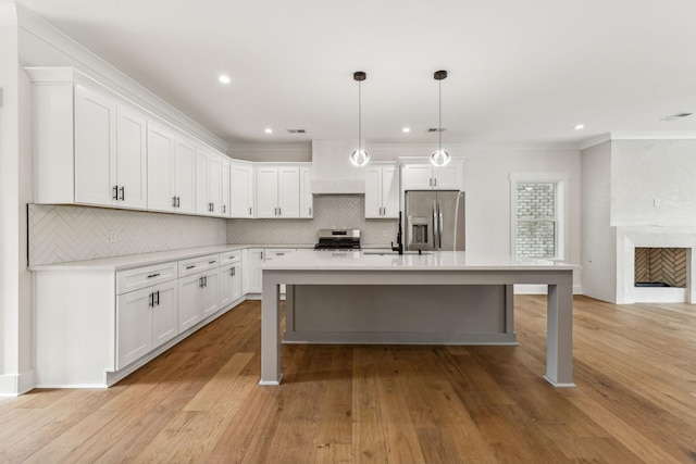 kitchen featuring hanging light fixtures, stainless steel appliances, white cabinets, a kitchen island, and light wood-type flooring