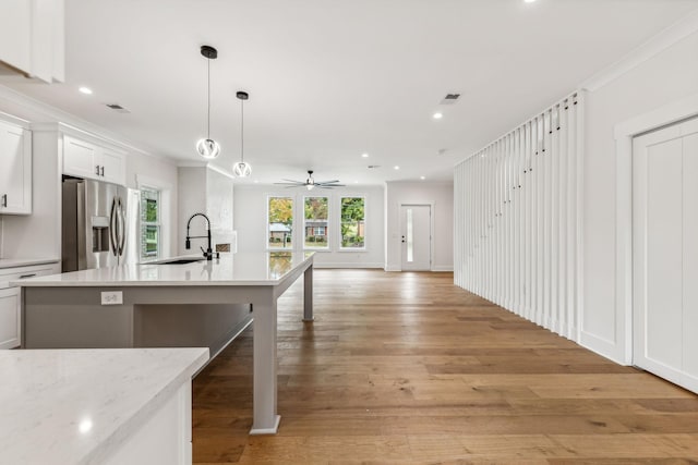 kitchen featuring pendant lighting, white cabinetry, sink, stainless steel fridge, and crown molding