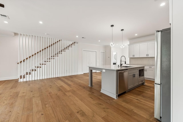 kitchen with appliances with stainless steel finishes, white cabinetry, sink, hanging light fixtures, and a kitchen island with sink