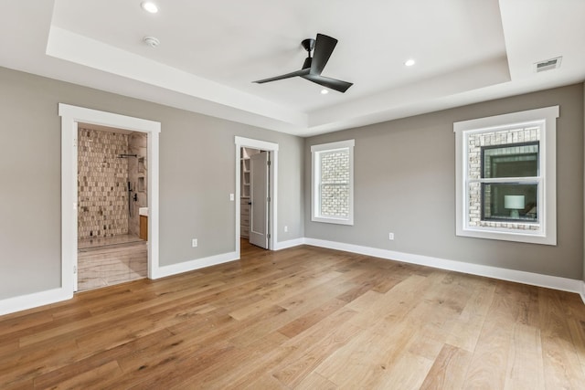 unfurnished bedroom featuring ensuite bath, a tray ceiling, light hardwood / wood-style flooring, and a spacious closet