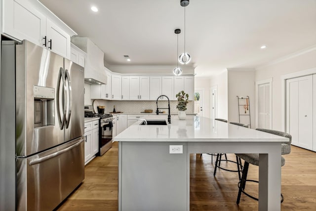 kitchen with sink, premium range hood, hanging light fixtures, stainless steel appliances, and an island with sink