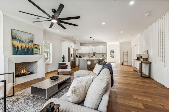 living room featuring sink, wood-type flooring, ornamental molding, a tile fireplace, and ceiling fan