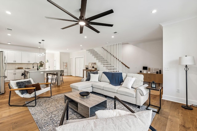 living room featuring sink, ornamental molding, light hardwood / wood-style floors, and ceiling fan