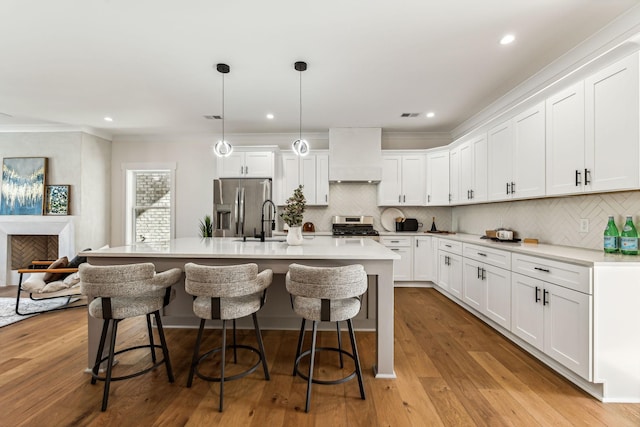 kitchen featuring pendant lighting, appliances with stainless steel finishes, white cabinetry, a center island with sink, and custom exhaust hood