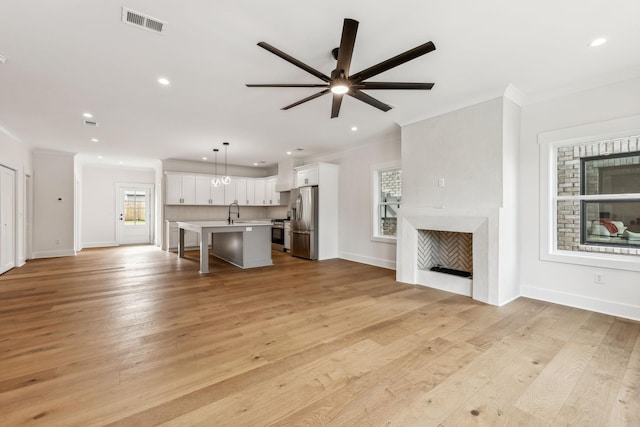 unfurnished living room with ceiling fan, ornamental molding, sink, and light wood-type flooring