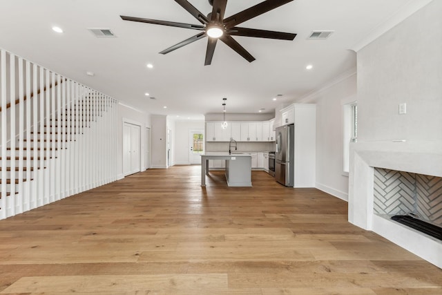 unfurnished living room featuring sink, a tiled fireplace, ornamental molding, ceiling fan, and light hardwood / wood-style floors