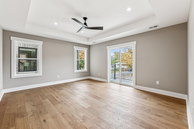 unfurnished room with ceiling fan, a tray ceiling, and light hardwood / wood-style flooring