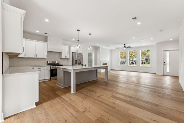 kitchen with stainless steel appliances, an island with sink, hanging light fixtures, and white cabinets