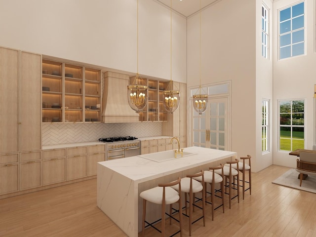 kitchen with a breakfast bar, pendant lighting, custom exhaust hood, light brown cabinets, and light hardwood / wood-style flooring