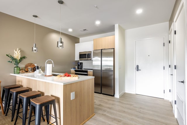 kitchen featuring pendant lighting, sink, stainless steel appliances, a center island with sink, and light wood-type flooring