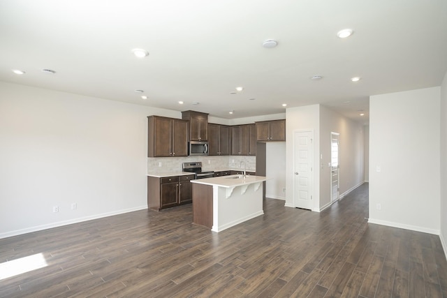 kitchen with sink, dark hardwood / wood-style flooring, an island with sink, stainless steel appliances, and decorative backsplash