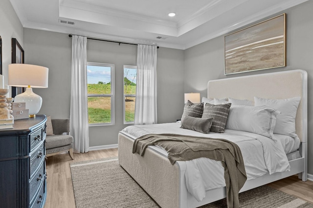 bedroom featuring ornamental molding, a raised ceiling, and light wood-type flooring