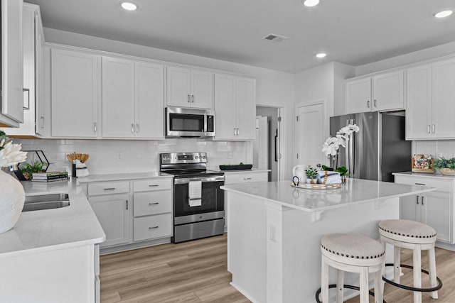 kitchen featuring a kitchen bar, a center island, appliances with stainless steel finishes, light hardwood / wood-style floors, and white cabinets