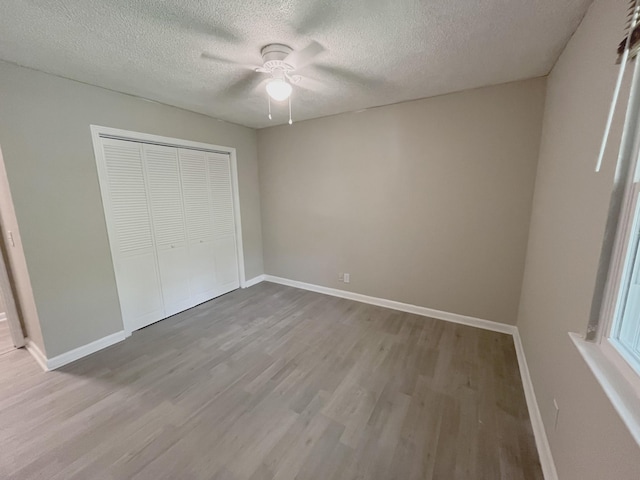 unfurnished bedroom with a textured ceiling, light hardwood / wood-style flooring, a closet, and ceiling fan