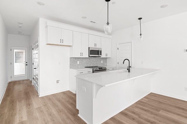 kitchen featuring sink, hanging light fixtures, stainless steel appliances, light hardwood / wood-style floors, and white cabinets