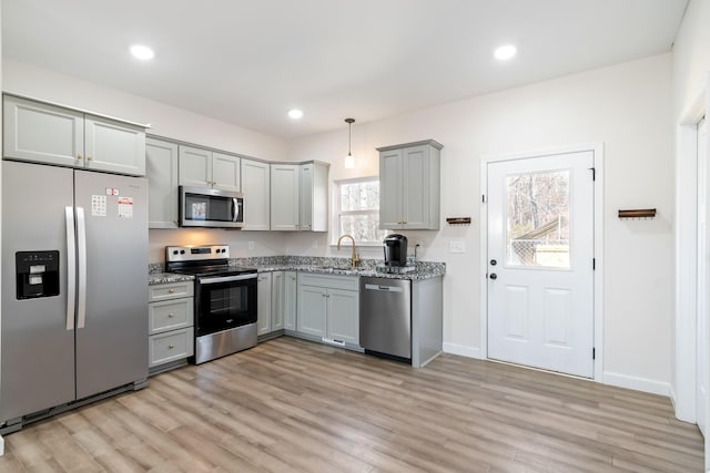 kitchen featuring pendant lighting, sink, light hardwood / wood-style floors, stainless steel appliances, and light stone countertops