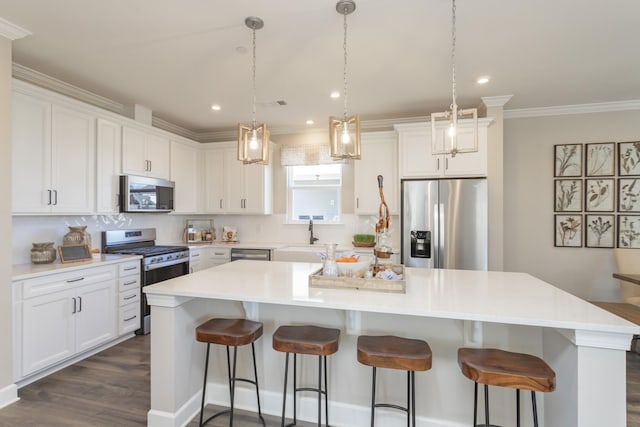 kitchen with a kitchen island, appliances with stainless steel finishes, pendant lighting, white cabinetry, and decorative backsplash