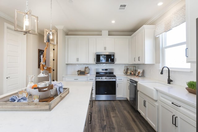 kitchen featuring pendant lighting, sink, crown molding, white cabinetry, and stainless steel appliances