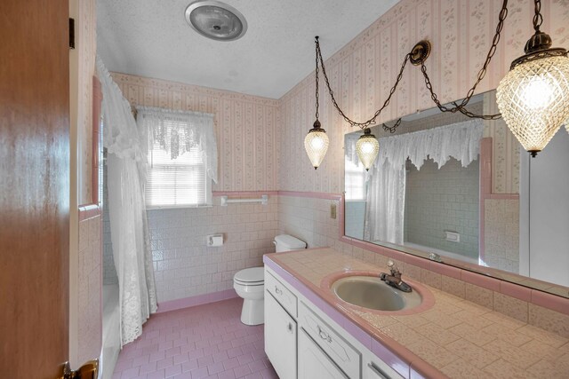 full bathroom featuring tile walls, vanity, shower / bath combination with curtain, a textured ceiling, and toilet