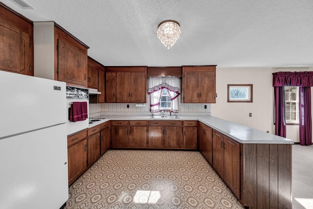 kitchen featuring sink, backsplash, white appliances, kitchen peninsula, and a textured ceiling