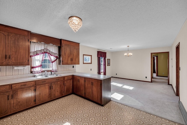 kitchen with pendant lighting, sink, a textured ceiling, kitchen peninsula, and a chandelier