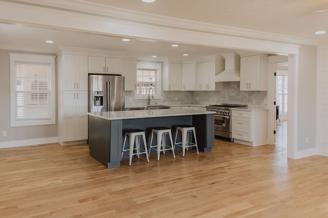 kitchen featuring a breakfast bar, white cabinetry, a center island, stainless steel appliances, and wall chimney range hood