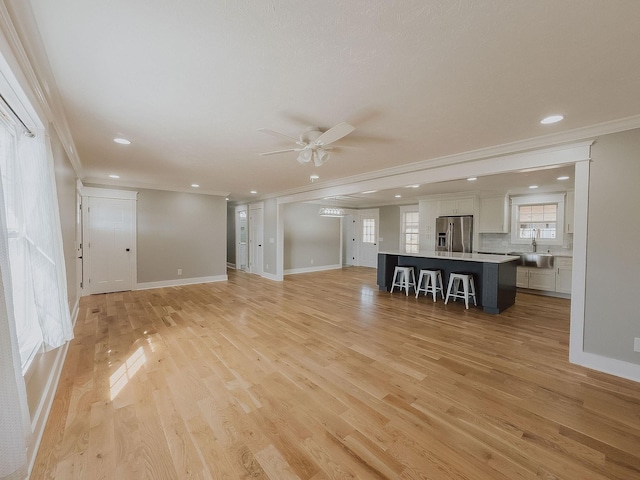 unfurnished living room with ornamental molding, sink, ceiling fan, and light wood-type flooring