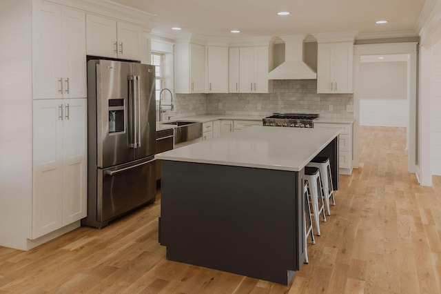 kitchen featuring sink, white cabinetry, high quality fridge, a kitchen island, and wall chimney exhaust hood