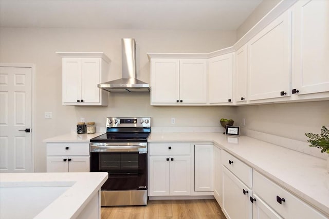 kitchen featuring white cabinetry, wall chimney range hood, stainless steel electric range, and light wood-type flooring