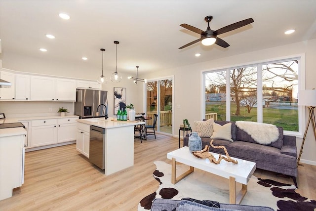 kitchen featuring stainless steel appliances, hanging light fixtures, a center island with sink, and white cabinets