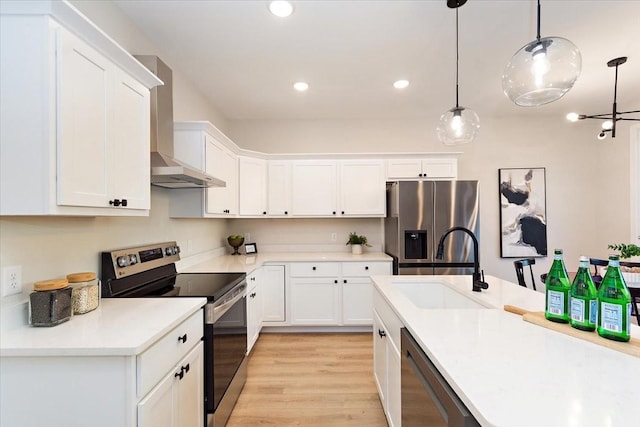 kitchen featuring wall chimney exhaust hood, white cabinetry, appliances with stainless steel finishes, and decorative light fixtures