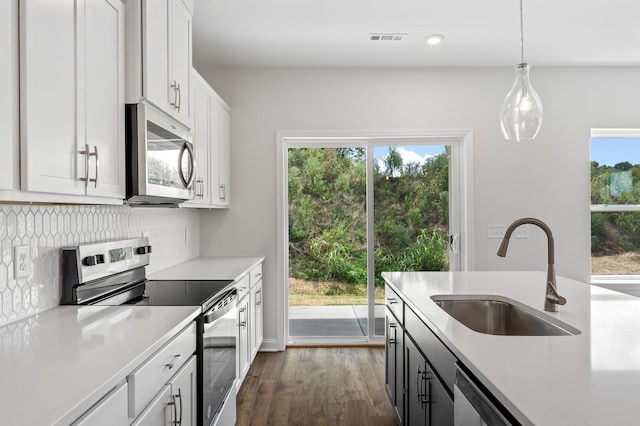 kitchen featuring appliances with stainless steel finishes, decorative light fixtures, white cabinetry, sink, and dark wood-type flooring