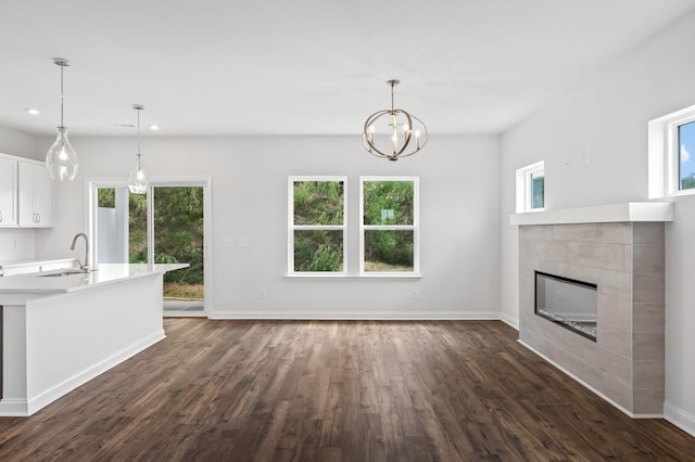 unfurnished living room with an inviting chandelier, sink, dark wood-type flooring, and a fireplace