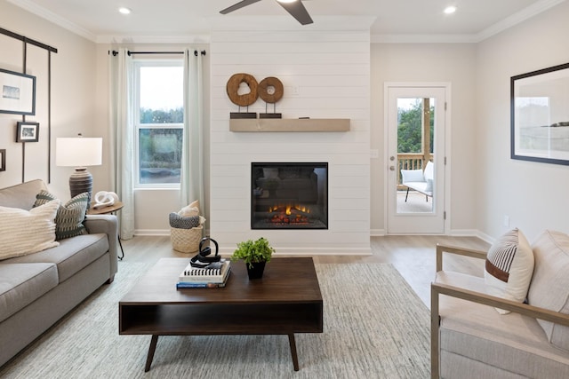 living room with crown molding, a wealth of natural light, a fireplace, and light hardwood / wood-style flooring