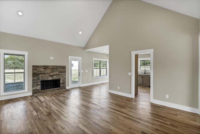 unfurnished living room with a stone fireplace, dark wood-type flooring, sink, and high vaulted ceiling