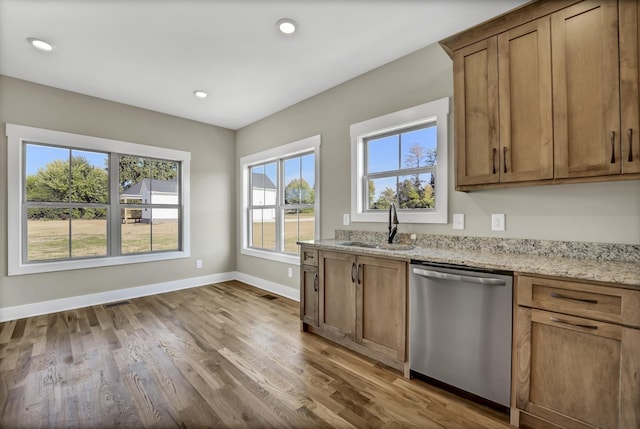 kitchen with light stone counters, dishwasher, sink, and hardwood / wood-style flooring