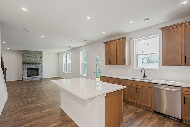 kitchen with sink, dishwasher, a center island, dark hardwood / wood-style flooring, and a stone fireplace