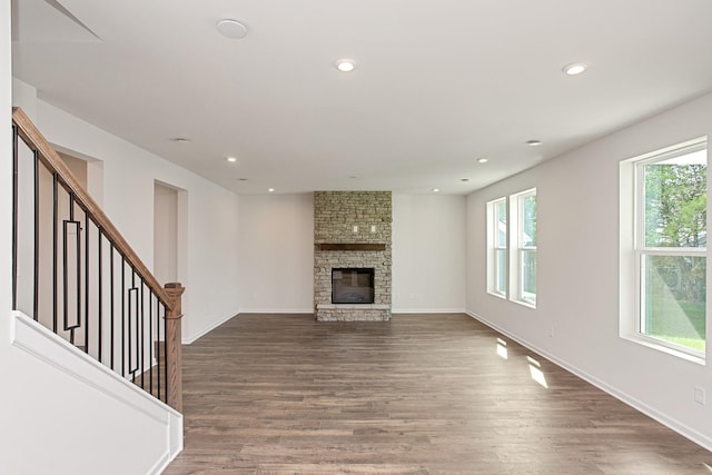 unfurnished living room with a stone fireplace and dark hardwood / wood-style floors