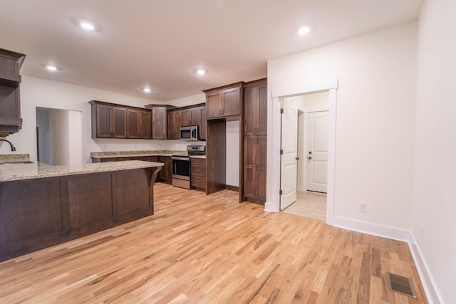 kitchen featuring appliances with stainless steel finishes, dark brown cabinetry, light stone countertops, kitchen peninsula, and light wood-type flooring