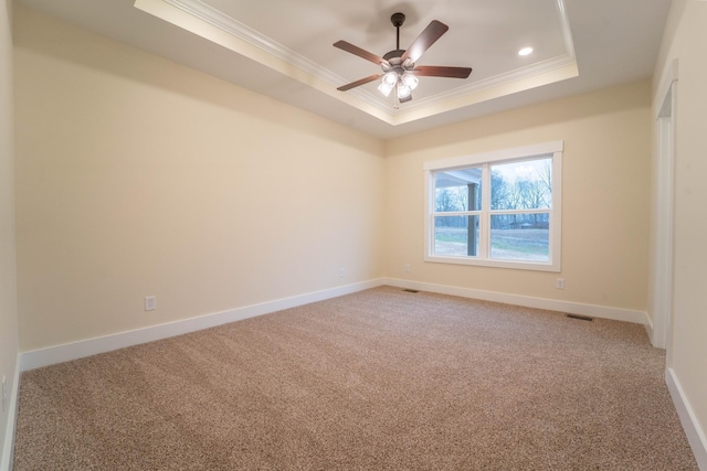 empty room with a raised ceiling, ornamental molding, and carpet floors